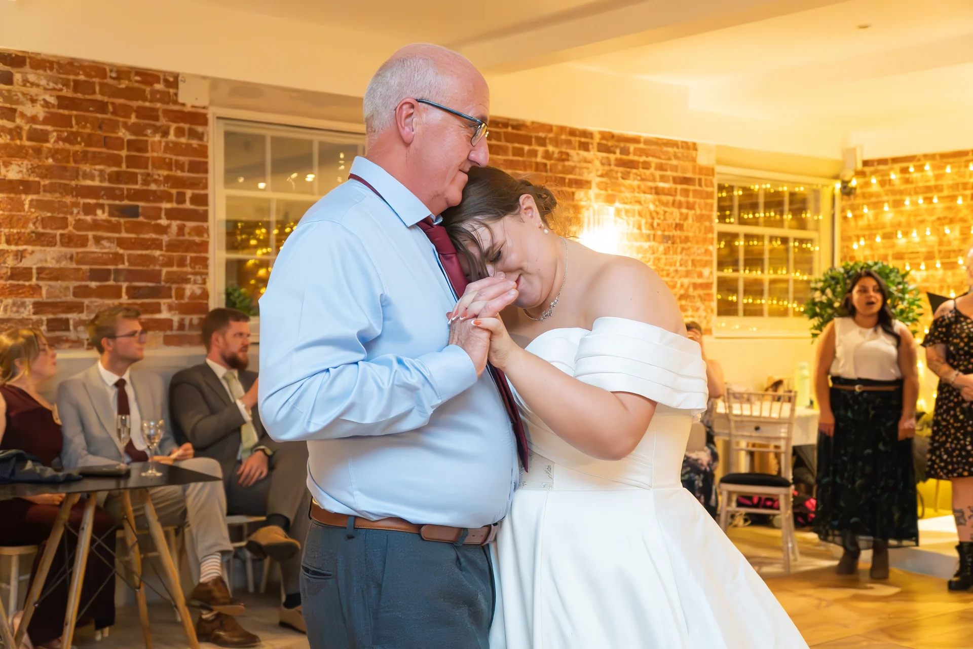 A smiling bride shares a tender father daughter dance with her father in an exposed brick venue during the wedding reception.