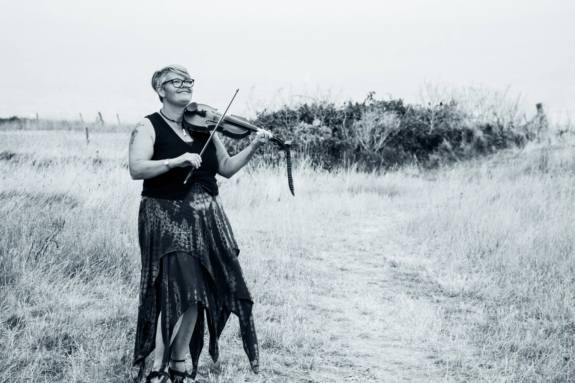 A musician plays the violin outdoors in a grassy meadow during a wedding celebration.