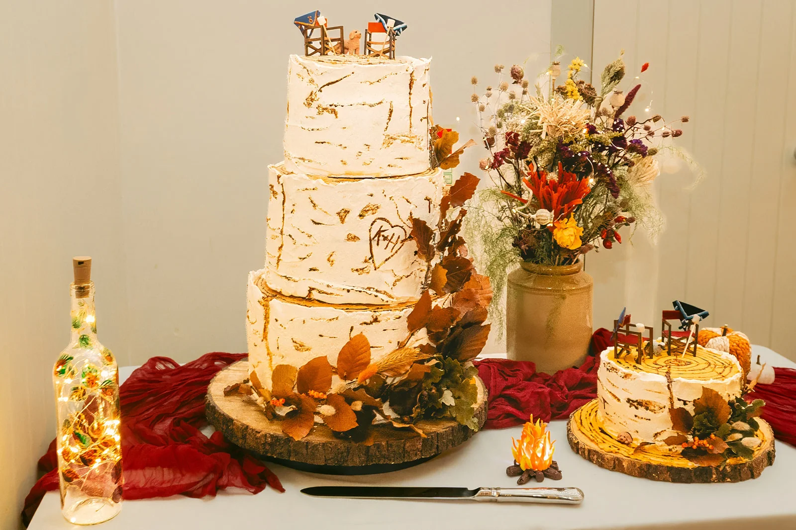 A stunning three-tiered wedding cake decorated with birch-bark textured buttercream, autumn leaves, and a custom topper sits on a rustic wood slice.