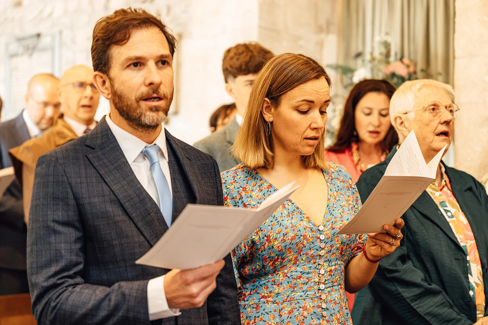 Wedding guests in a church hold service sheets and sing together during the ceremony.