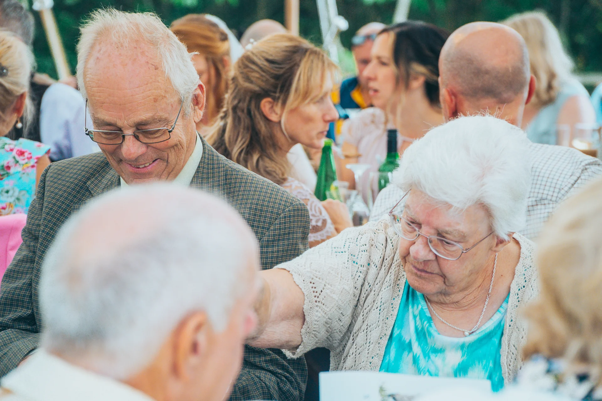 Elderly wedding guests enjoying a warm conversation during the wedding reception dinner inside a marquee.
