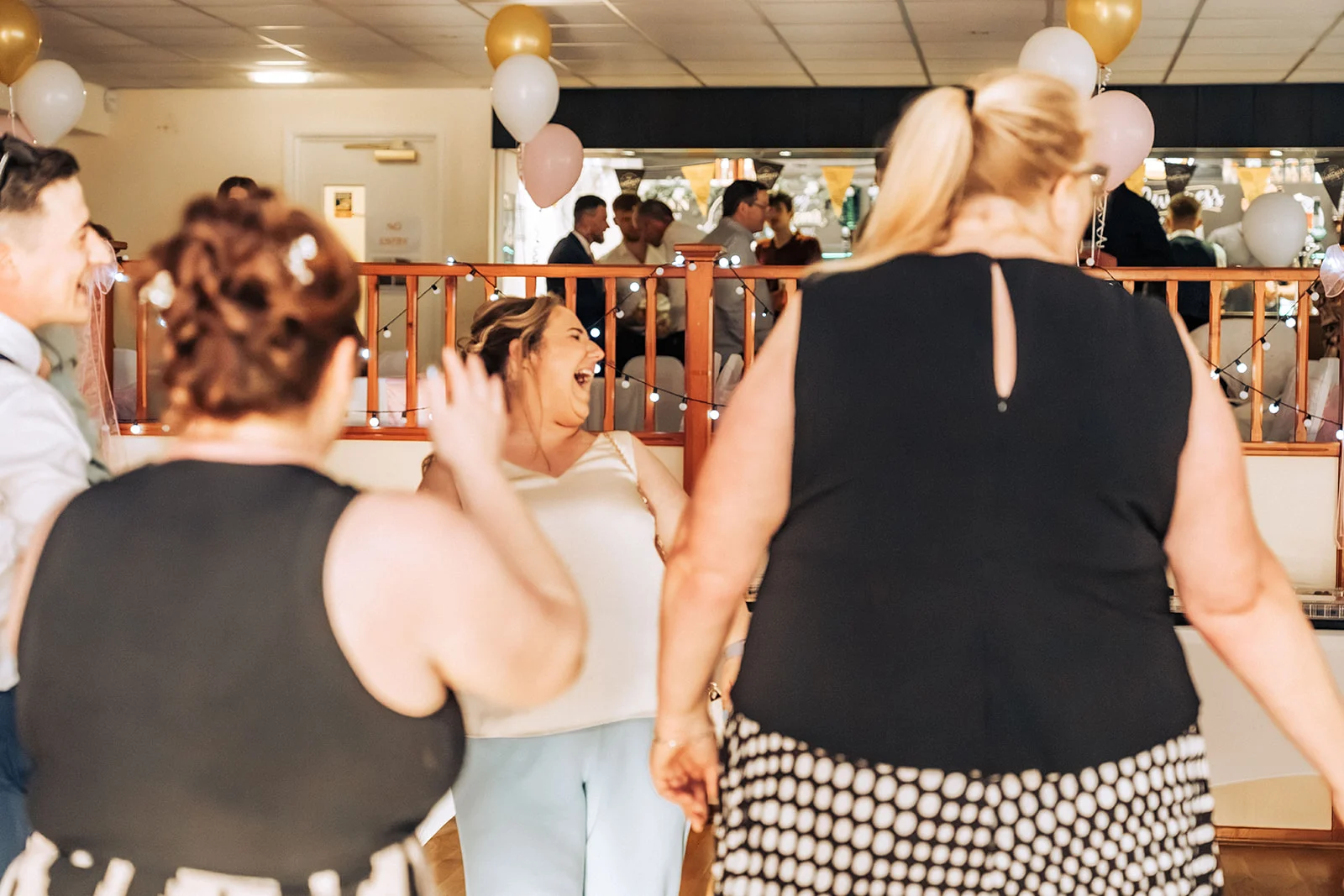 Wedding guests laugh and dance joyfully together during a lively evening reception illuminated by string lights.