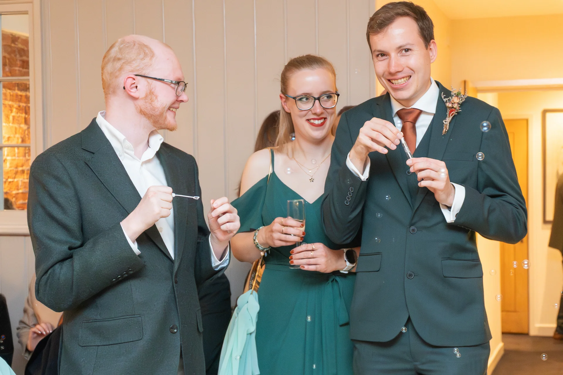 Wedding guests smiling and laughing as they blow bubbles together during the drinks reception.