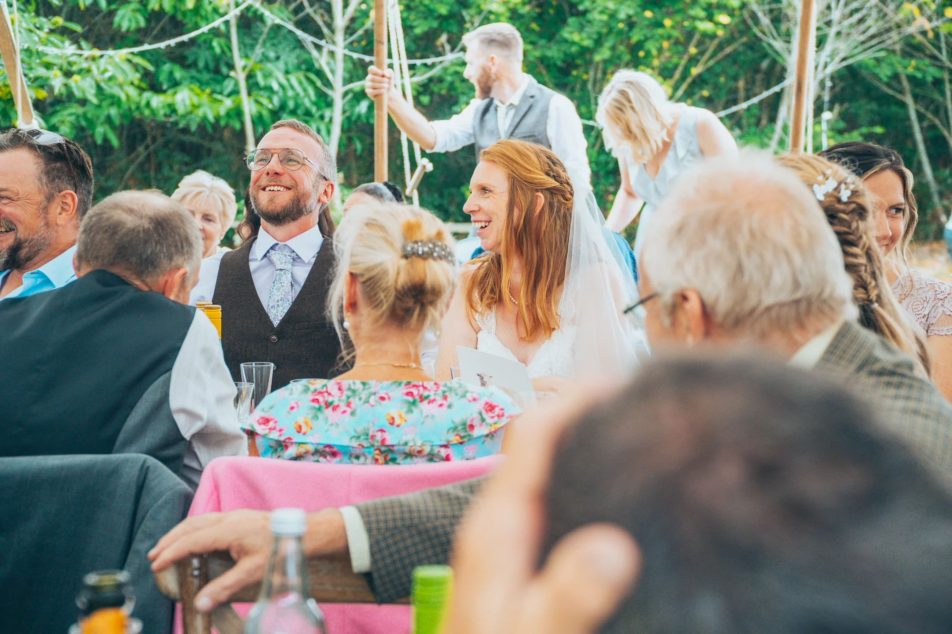 The bride and groom and their wedding guests share a joyful, laughter-filled moment during the speeches at a marquee reception.
