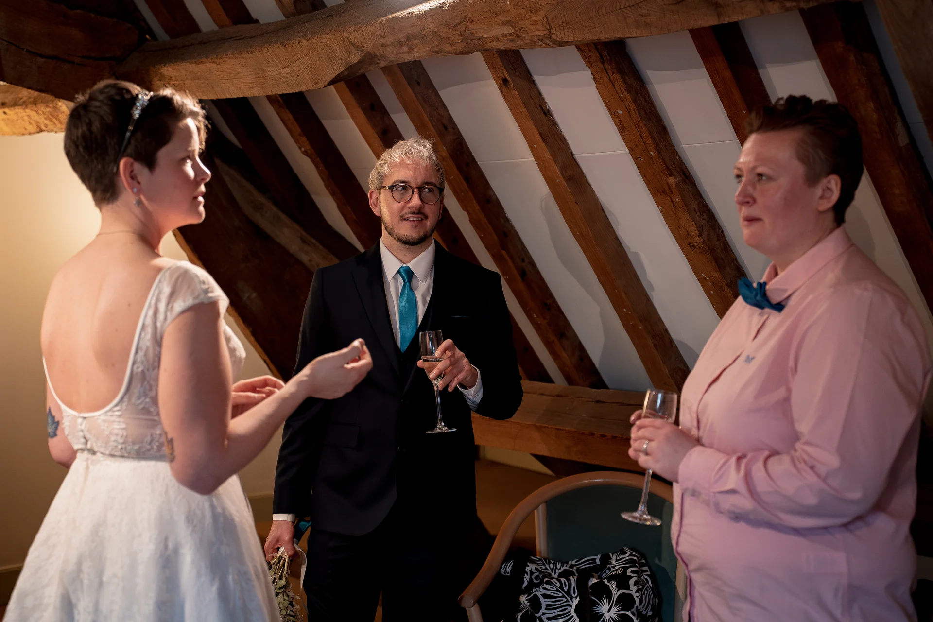 Guests enjoy drinks during a reception inside a rustic barn featuring vaulted ceilings and exposed wooden rafters.