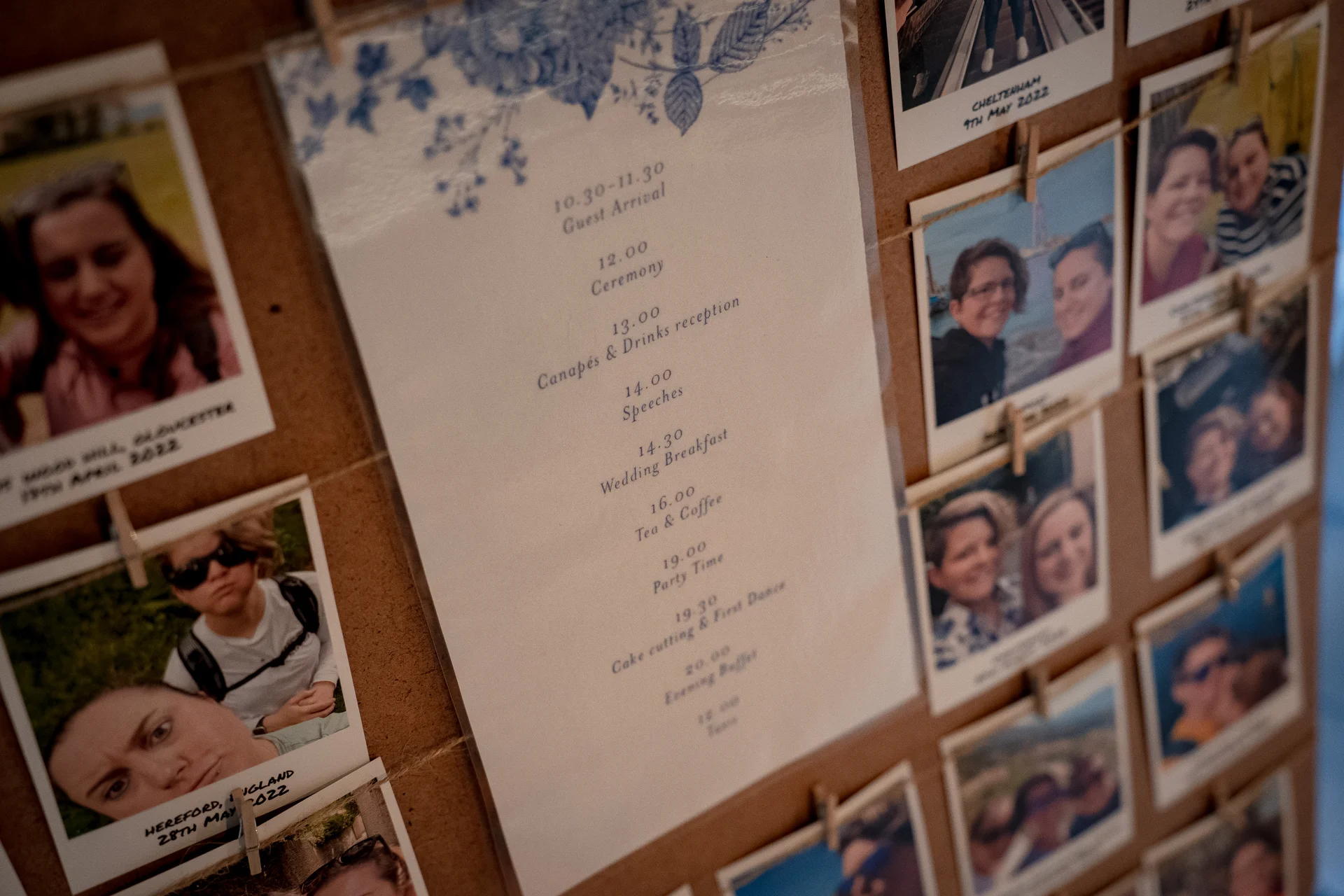 An eye-level close up shot of a wedding order of the day sign displayed alongside polaroid photographs on a cork board.