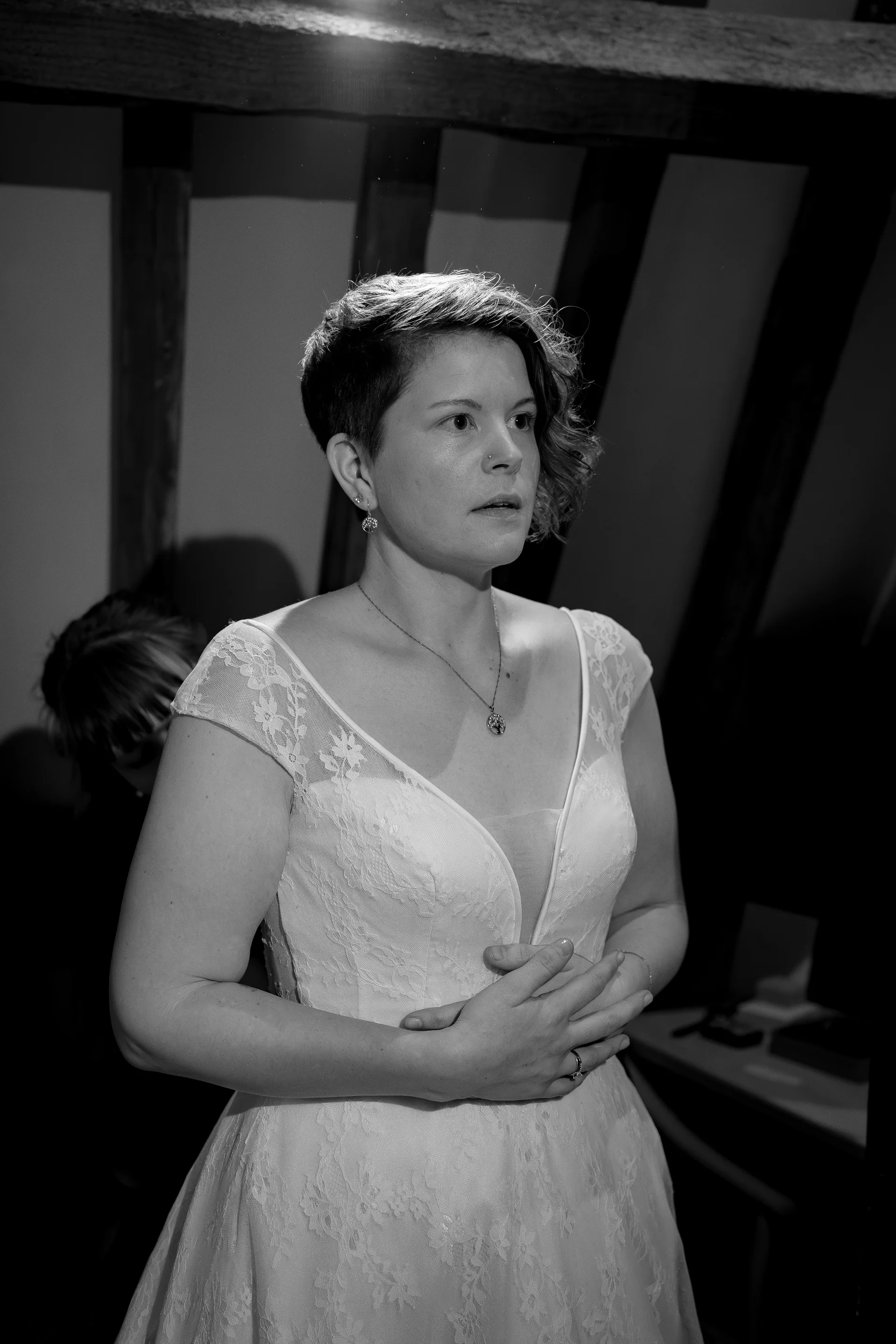 A stunning black and white portrait captures a bride with a modern undercut hairstyle during wedding preparations, wearing a lace gown with a plunging neckline inside a rustic room with exposed wooden beams.