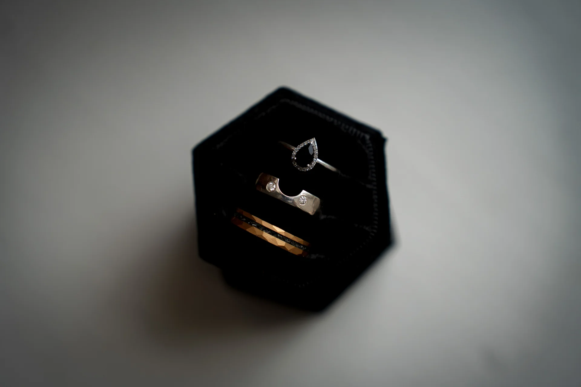 A close-up shot of three unique wedding and engagement rings displayed neatly inside a black hexagonal velvet ring box.
