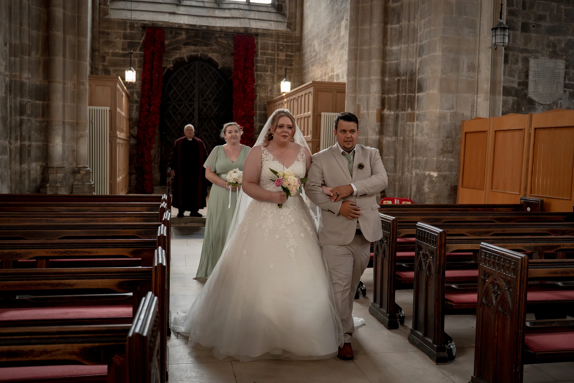 Newlyweds walk down the aisle together inside a historic stone church featuring wooden pews and soaring architectural columns.