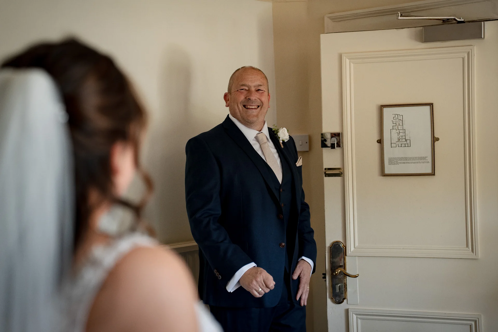 An emotional father of the bride wearing a navy three-piece suit smiles proudly as he shares a special first look moment with his daughter.
