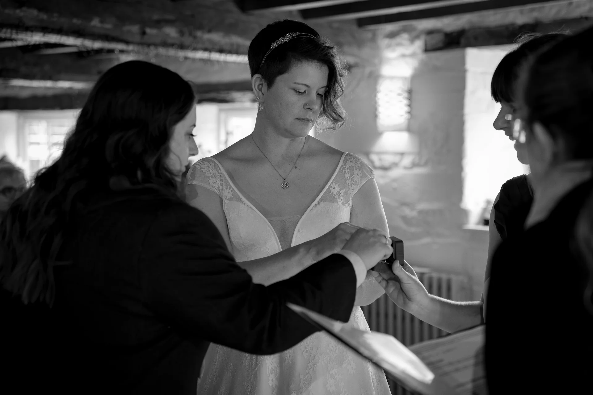 A couple exchanges rings during an intimate black and white indoor wedding ceremony surrounded by family and friends.
