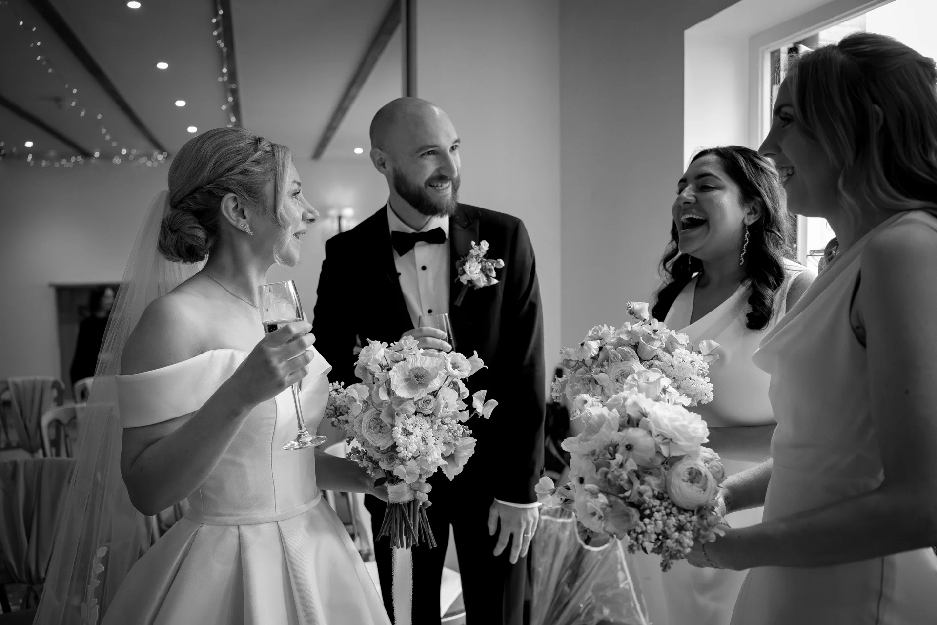 A newlywed couple sharing drinks and laughing joyfully with their bridesmaids during the wedding reception.