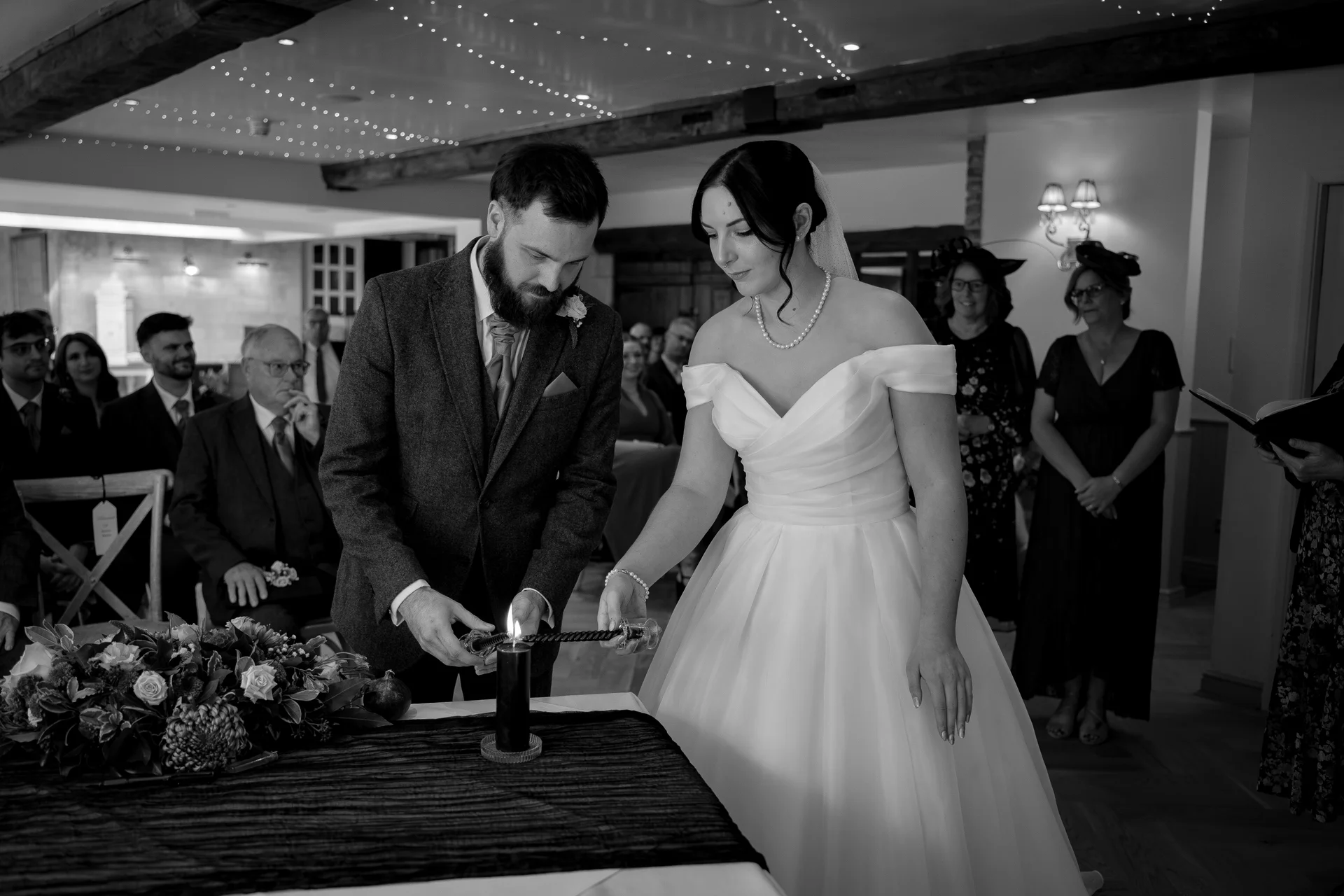 The bride and groom perform a unity candle lighting ceremony together in an indoor venue while guests watch from the pews.