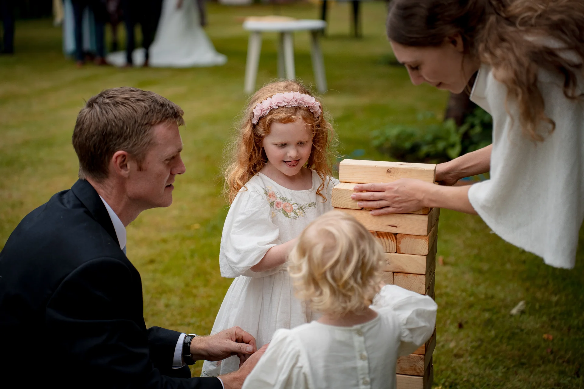 Guests and children happily play with a giant wooden tower game on the lawn during a wedding reception.