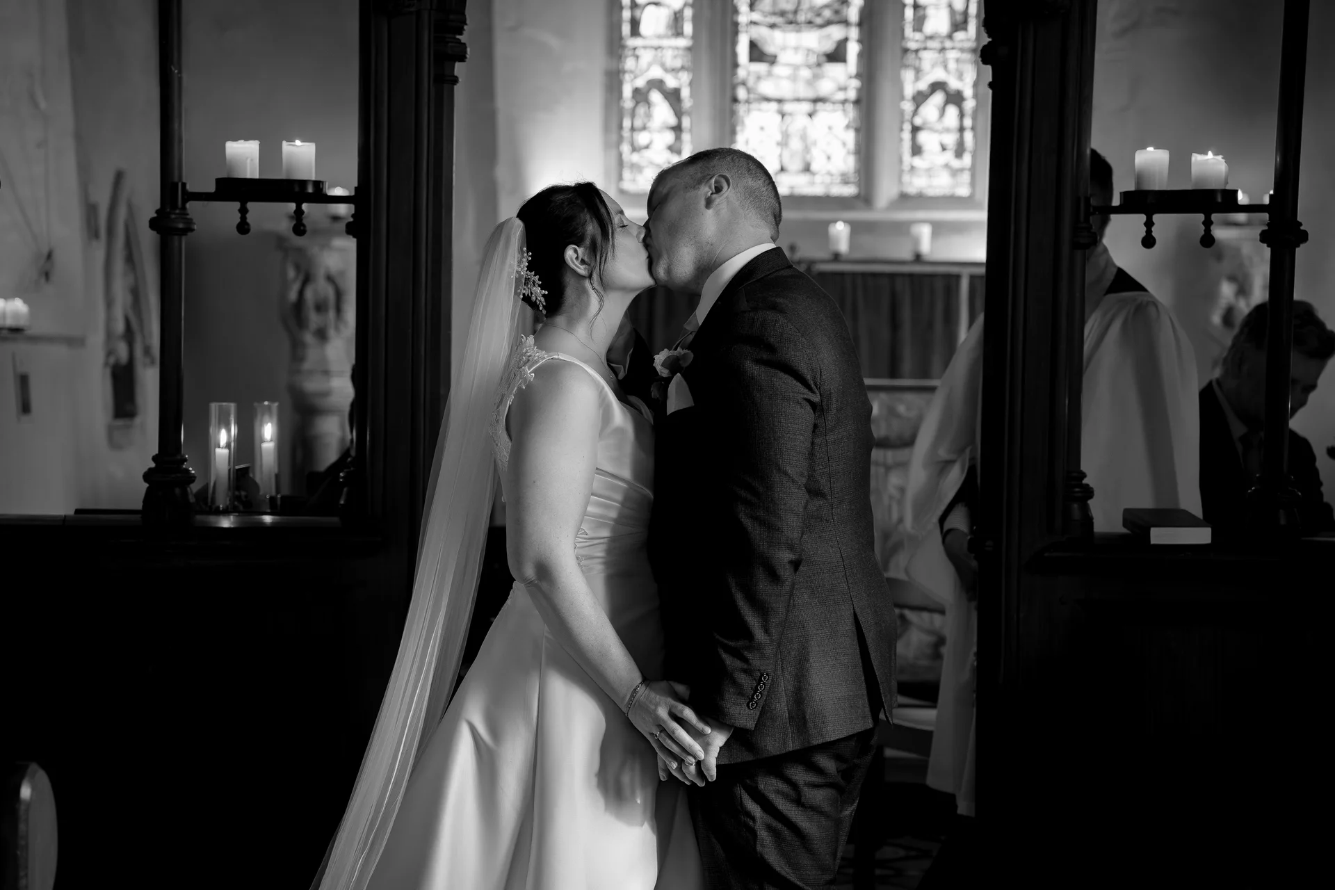The bride and groom share their first kiss at the altar inside a candlelit church during a traditional wedding ceremony.