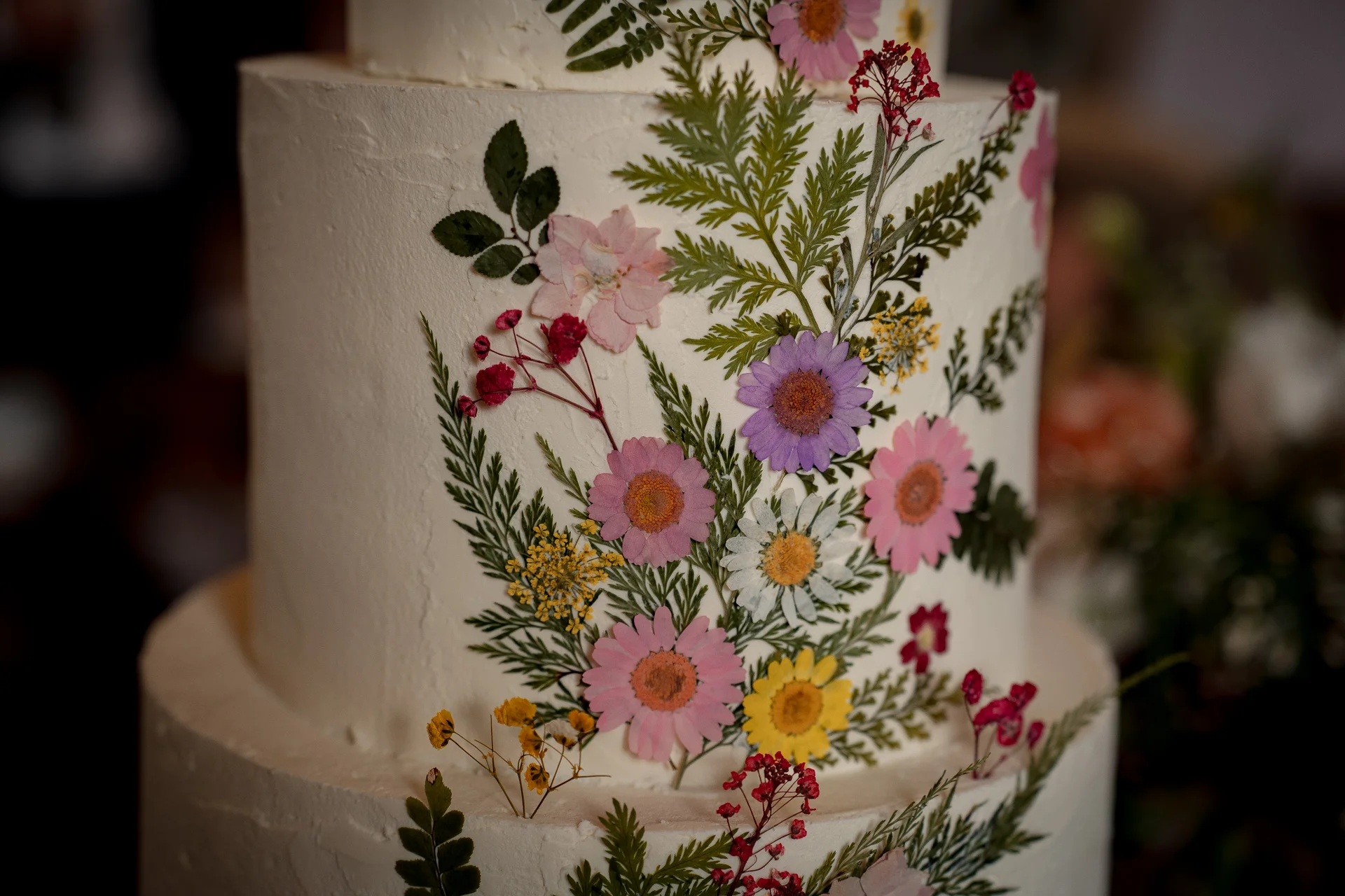 A close-up view of a tiered white buttercream wedding cake beautifully decorated with delicate pressed flowers and foliage.
