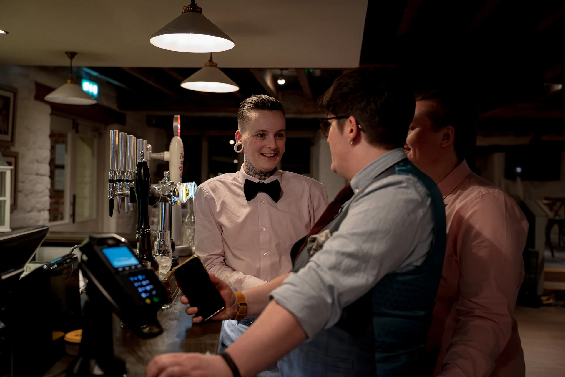 Guests enjoy drinks at the bar during a relaxed pub wedding reception, sharing a cheerful moment together.