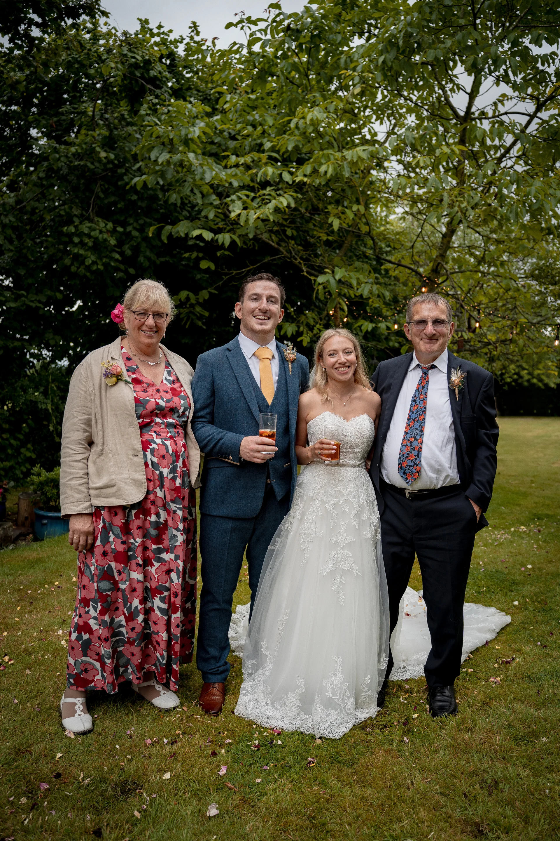 The newly married couple pose outdoors in a lush garden alongside family members during the drinks reception, holding glasses of Pimm's.
