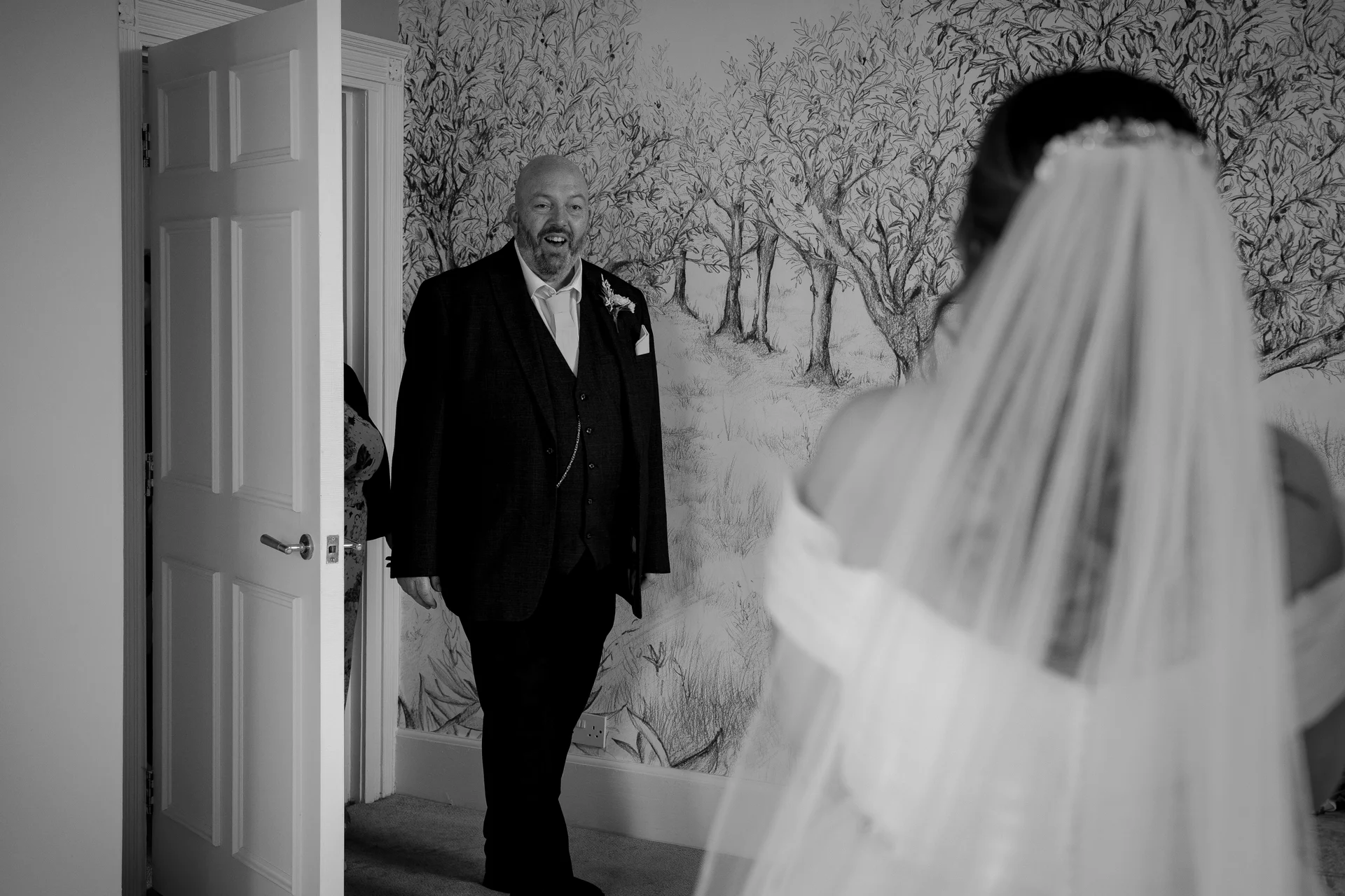 An emotional father beams with joy as he sees his daughter in her wedding dress and veil for the first time during bridal preparations.