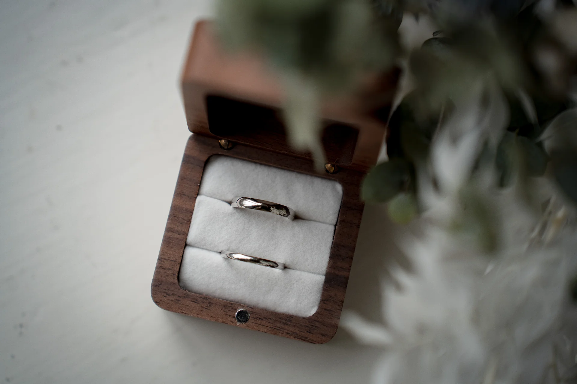 A close-up shot of two silver wedding bands resting neatly inside an open wooden ring box lined with white velvet.