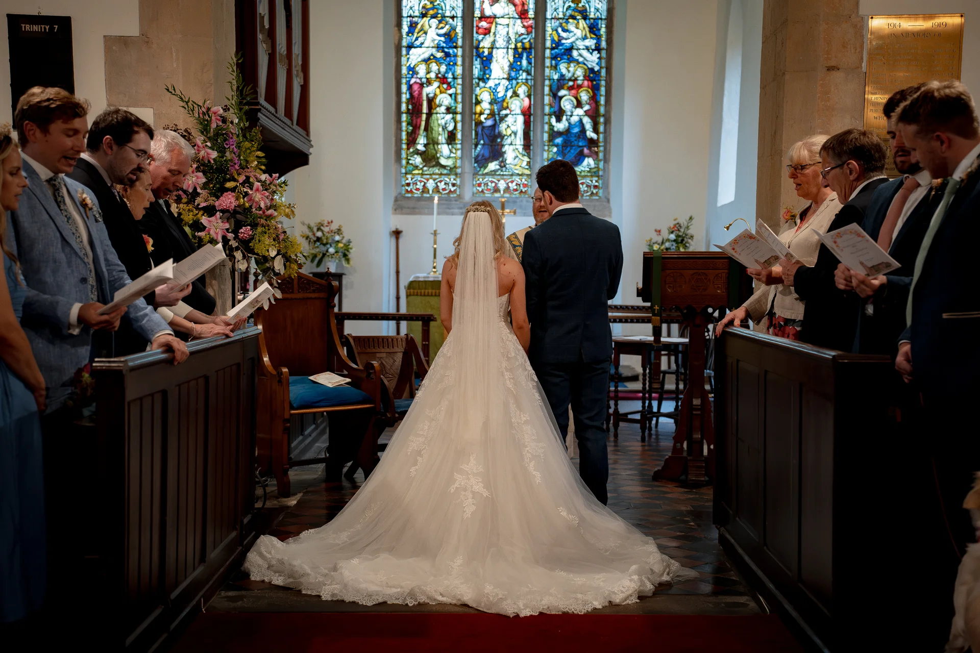 A bride in a lace gown with a long train and veil stands at the altar with the groom inside a traditional church during the wedding ceremony.