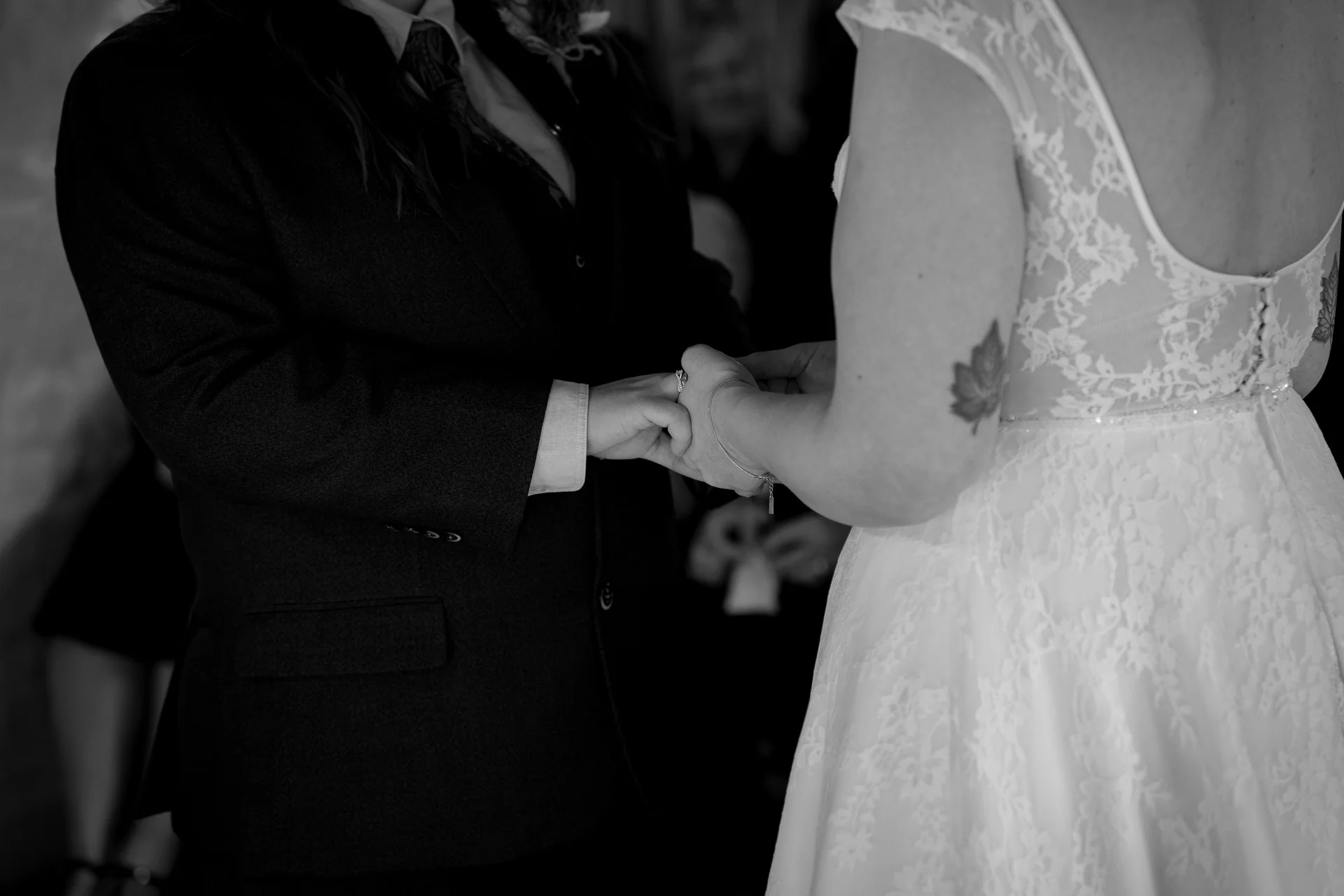 A close-up black and white shot of a couple exchanging wedding rings during their ceremony, featuring a detailed lace dress and a tailored suit.
