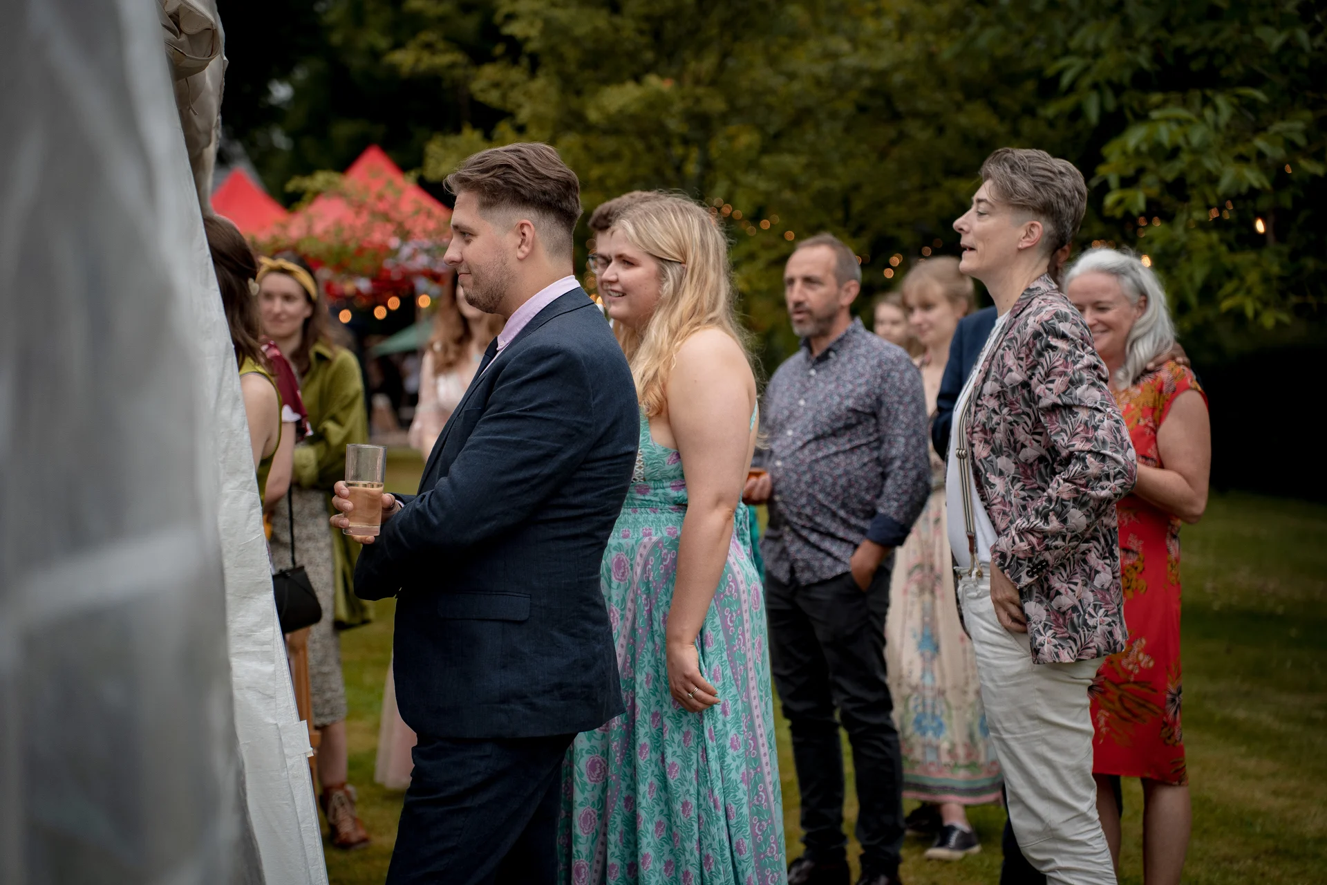 Wedding guests mingle outside near a marquee tent during a relaxed summer festival wedding reception.