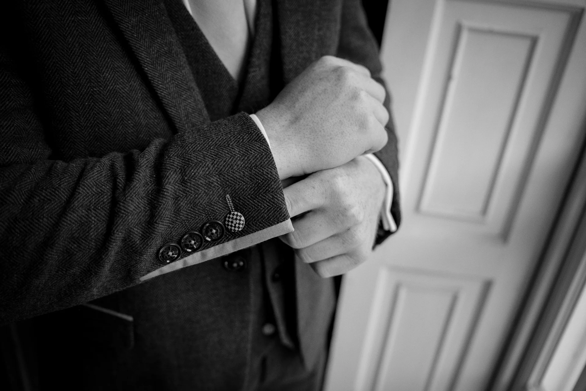 A groom adjusts his cuffs while wearing a textured tweed three-piece suit during morning preparations.