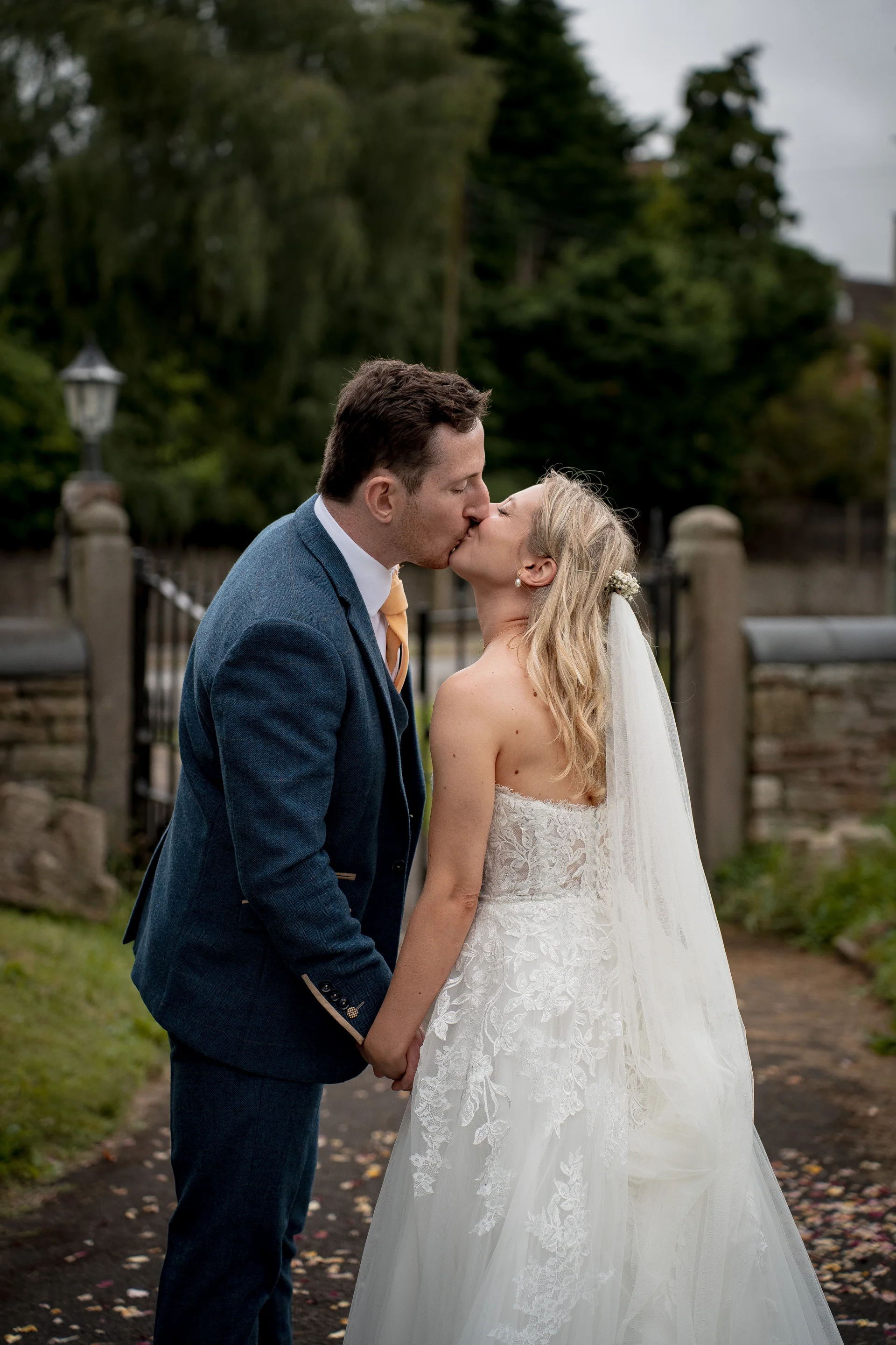 A bride and groom share a tender kiss outside an old stone entrance on their wedding day, surrounded by lush greenery.