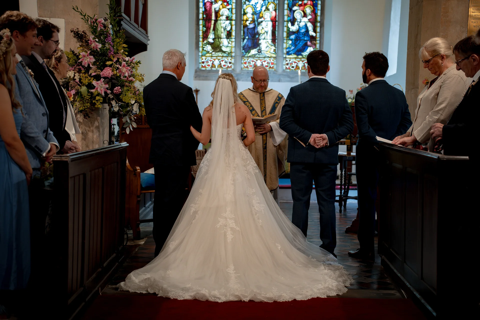 A bride with a dramatic cathedral train and veil stands at the altar inside a traditional church during the wedding ceremony.