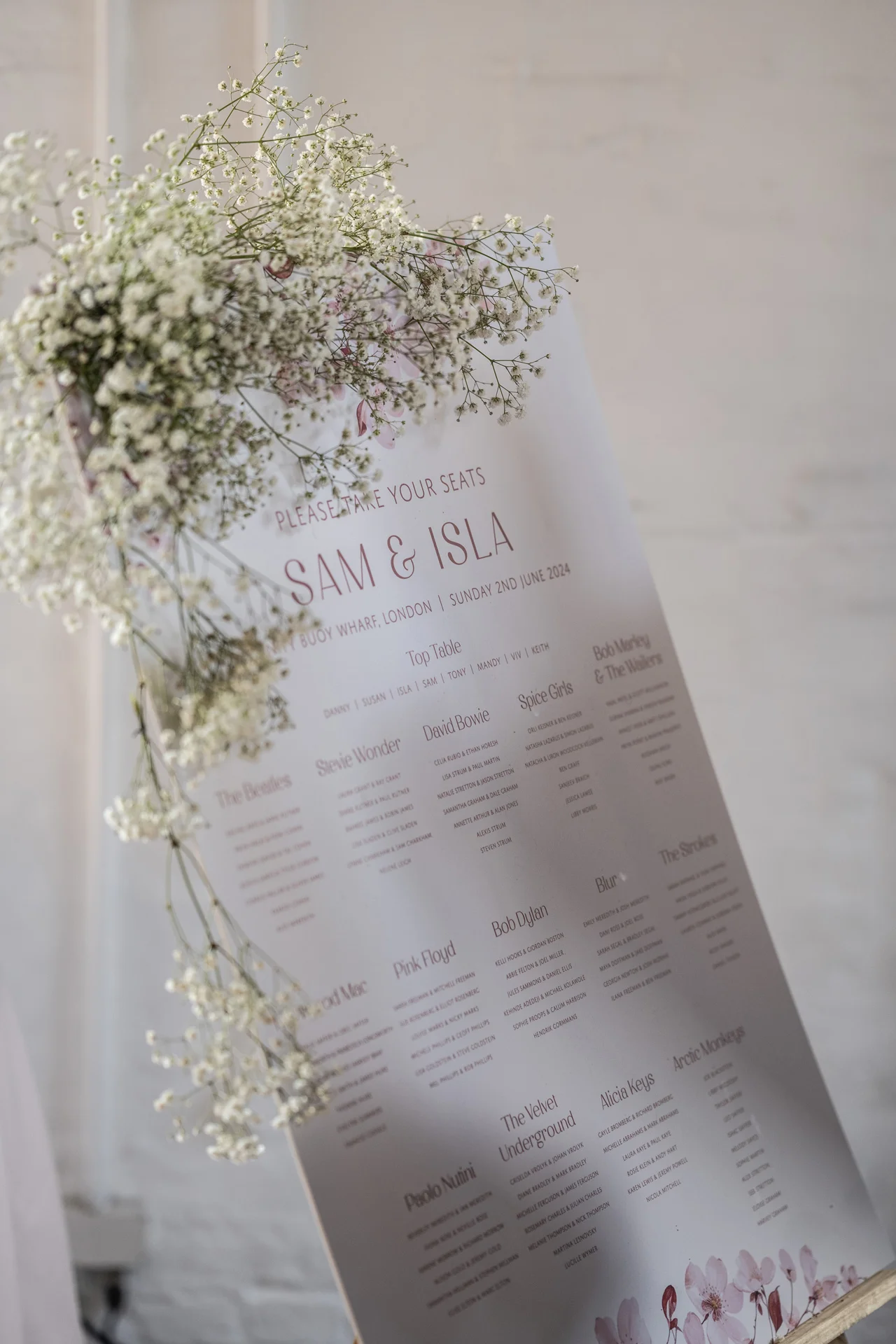 A modern minimalist wedding seating plan display is beautifully adorned with delicate gypsophila florals against an exposed white brick backdrop.
