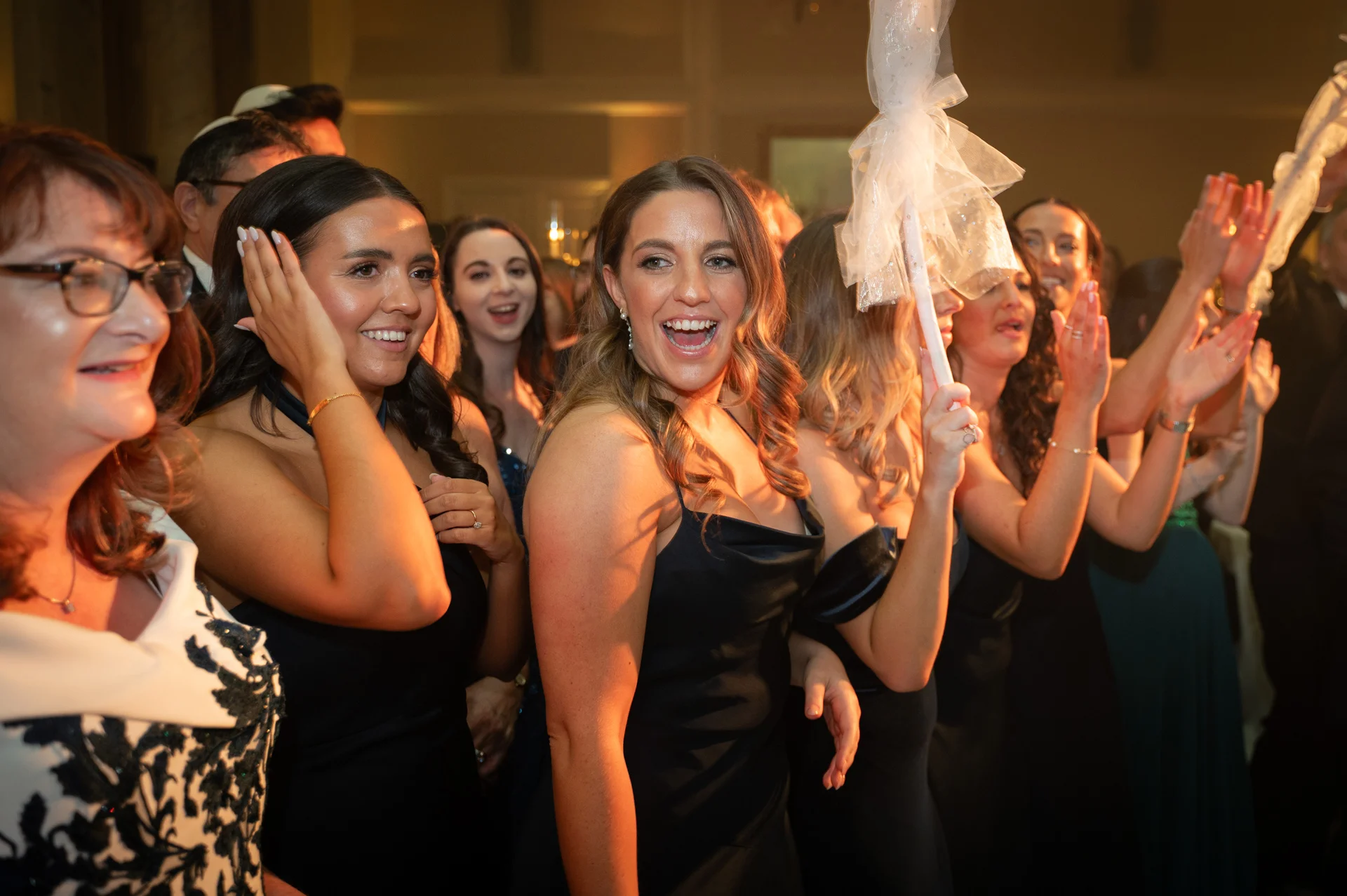 A lively group of wedding guests cheer and laugh with joy during an indoor evening celebration.