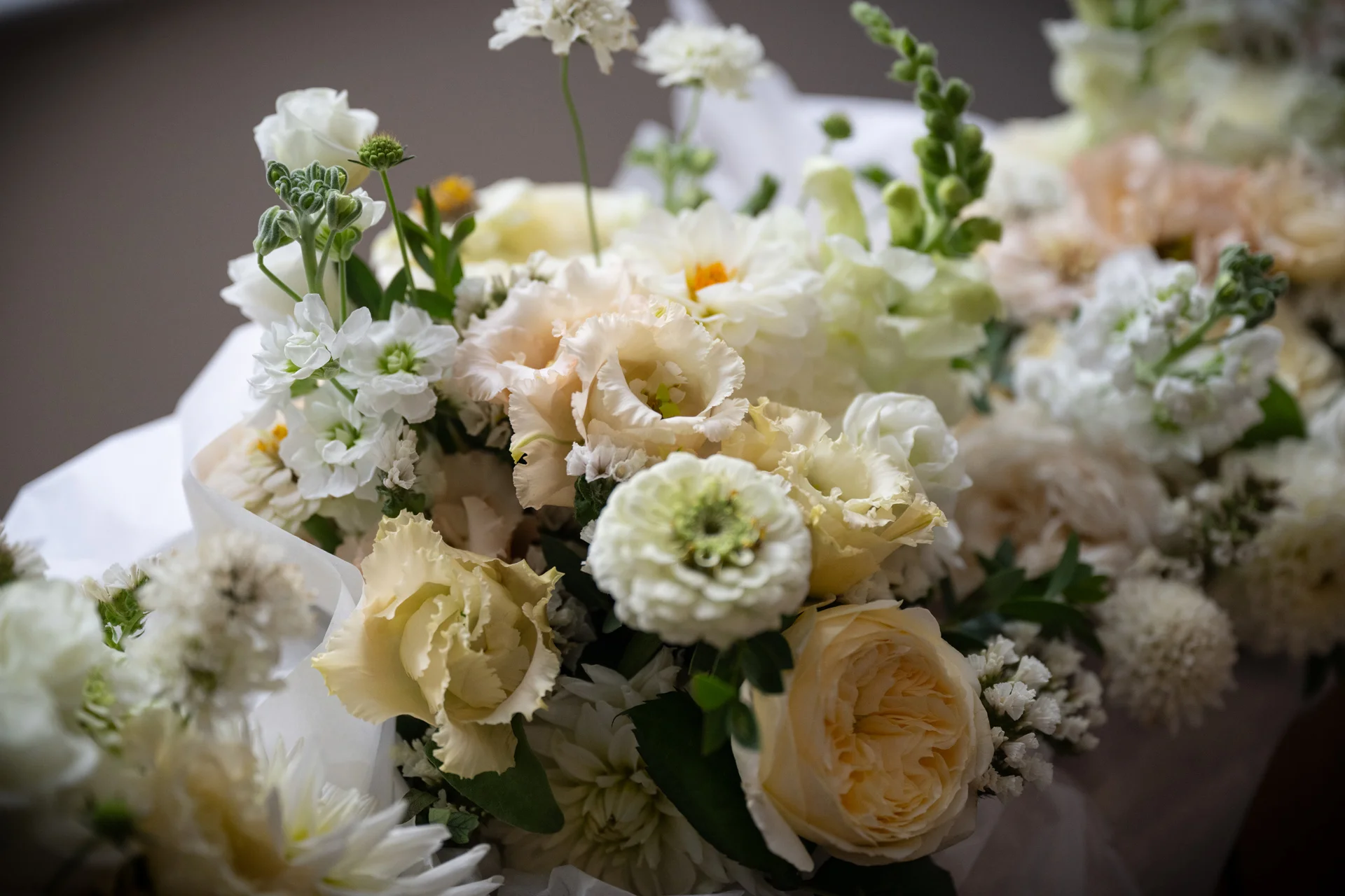A close-up view of an elegant wedding floral arrangement featuring a soft neutral palette of cream, ivory, and champagne roses and ranunculus.