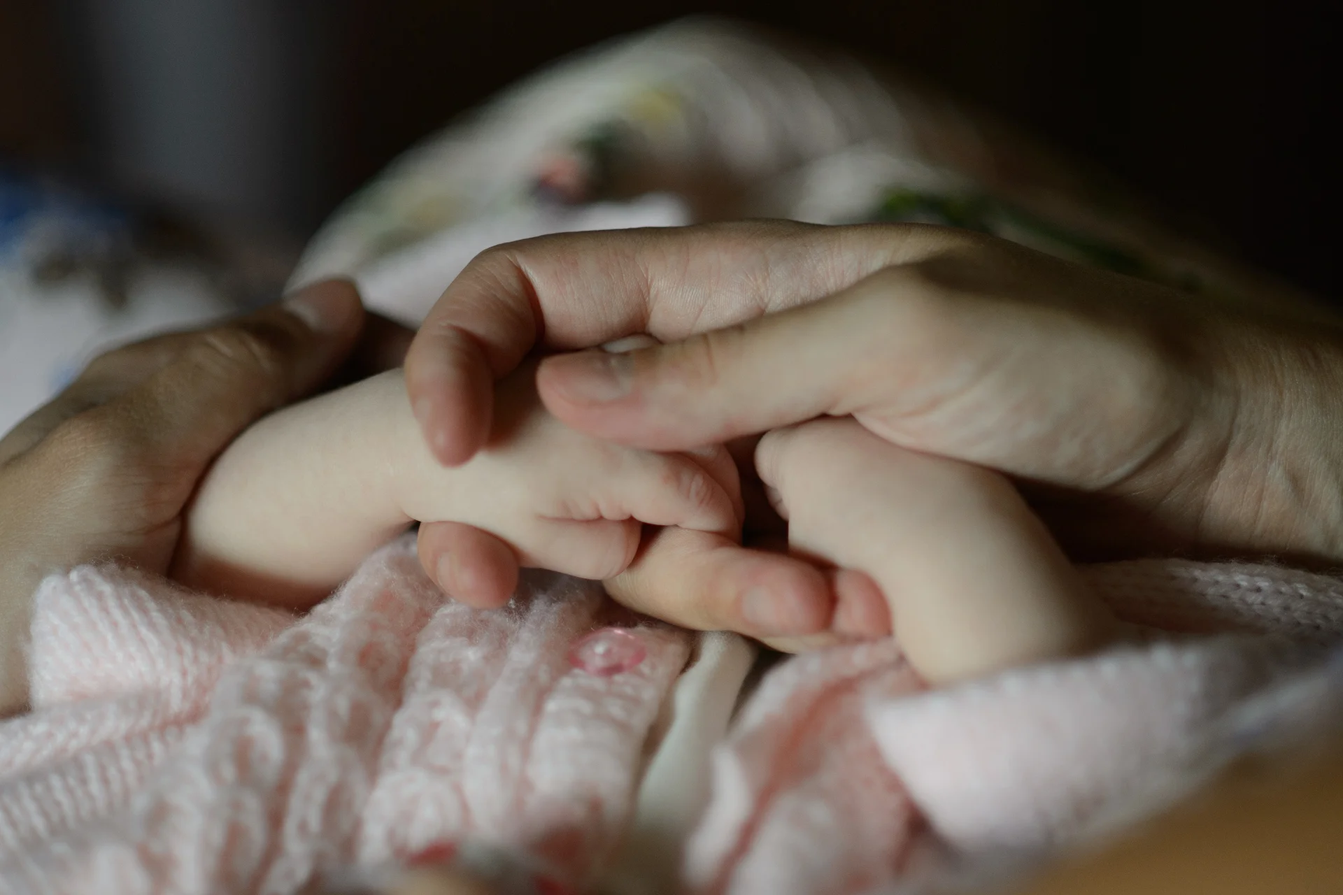 An adult hand gently holding a tiny baby's hand, capturing a tender and intimate moment of family connection.