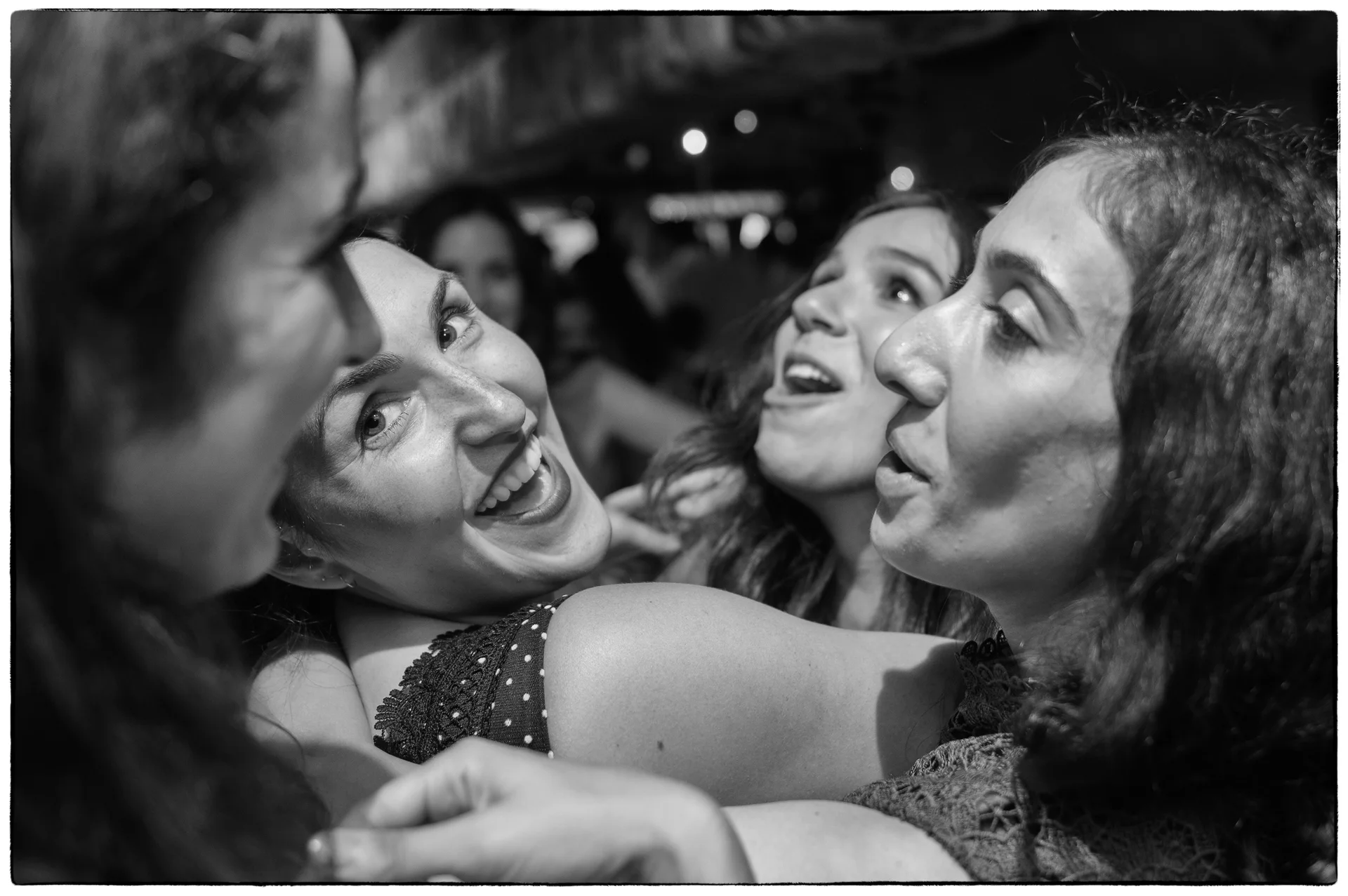 A candid black and white shot captures a group of wedding guests laughing and dancing closely together on the lively dance floor.
