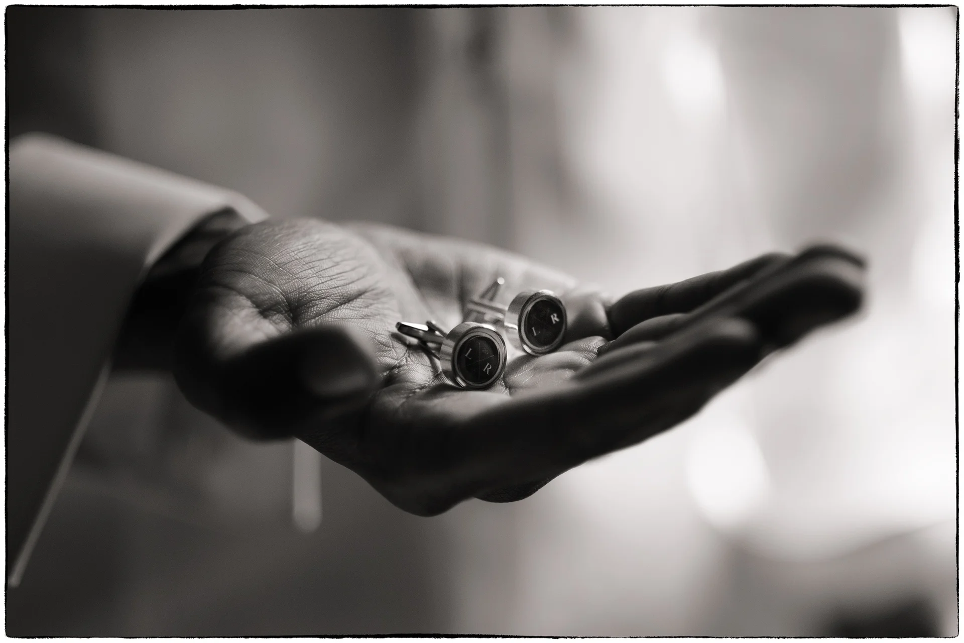 A close-up black and white shot of a groom holding a pair of personalised cufflinks in the palm of his hand during morning preparations.