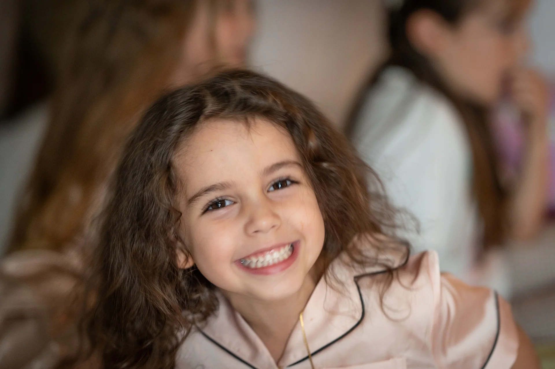 A young flower girl smiling brightly while wearing matching pyjamas during wedding morning preparations.