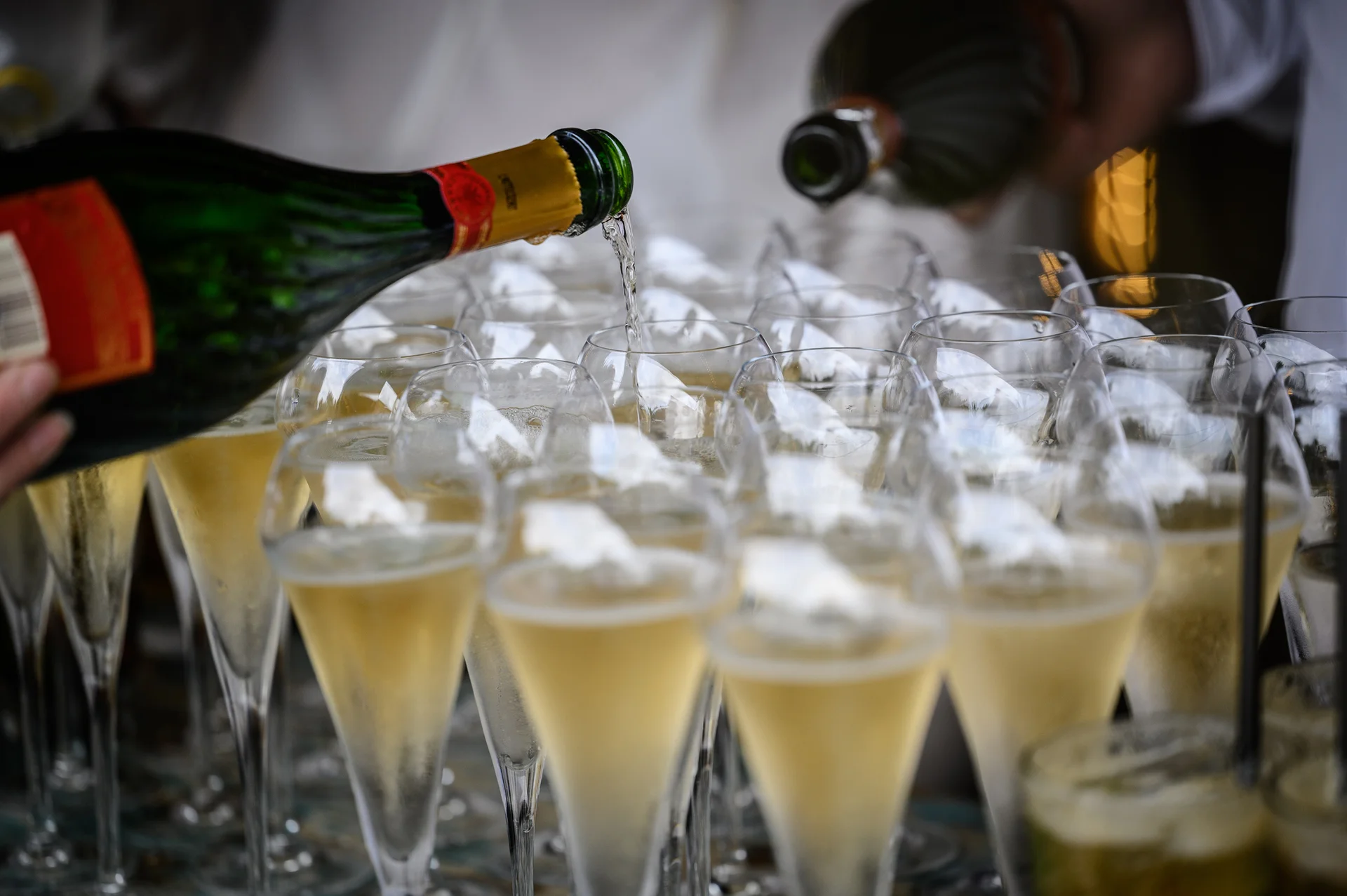 A close-up shot of a member of the service staff pouring champagne into a row of crystal flutes during a wedding drinks reception.