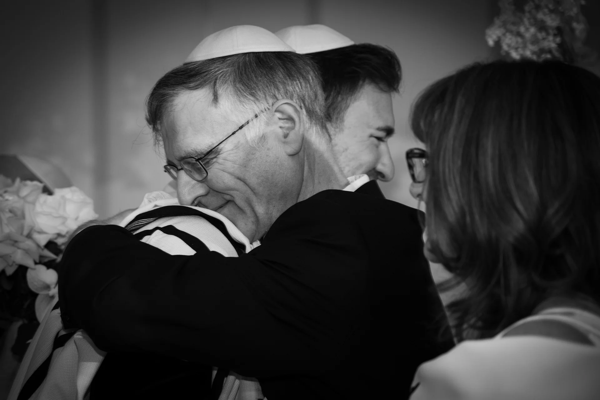An emotional black and white portrait captures a tender embrace between family members during a Jewish wedding ceremony.