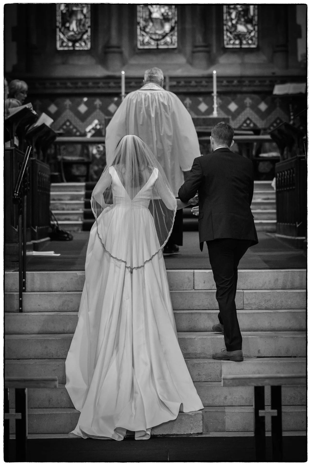A bride and groom walk hand in hand up the stone steps inside a historic church during their wedding ceremony.