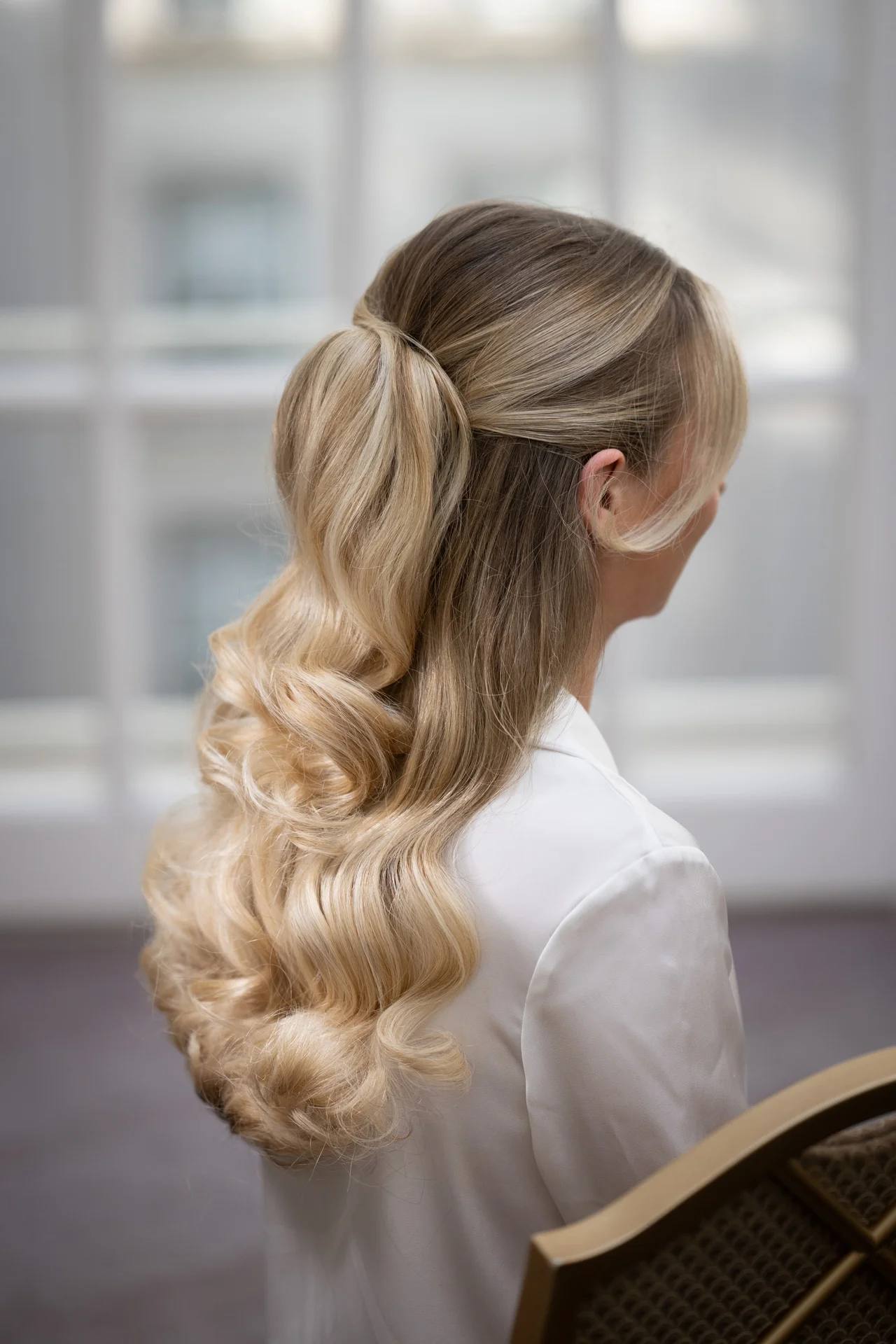 A close-up back view of a bride showcasing her elegant half-up half-down blonde hairstyle with soft waves during morning preparations.