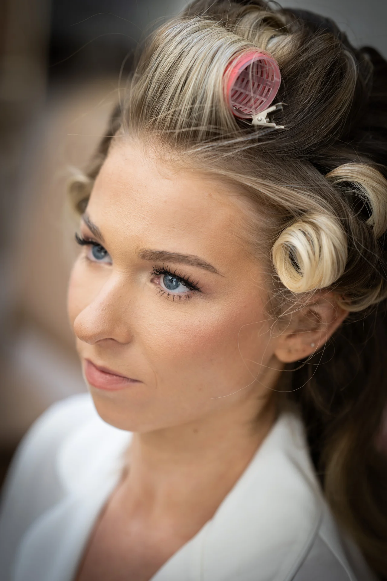 A close-up portrait of a bride during morning preparations, with hair rollers set in her blonde hair and soft bridal makeup.