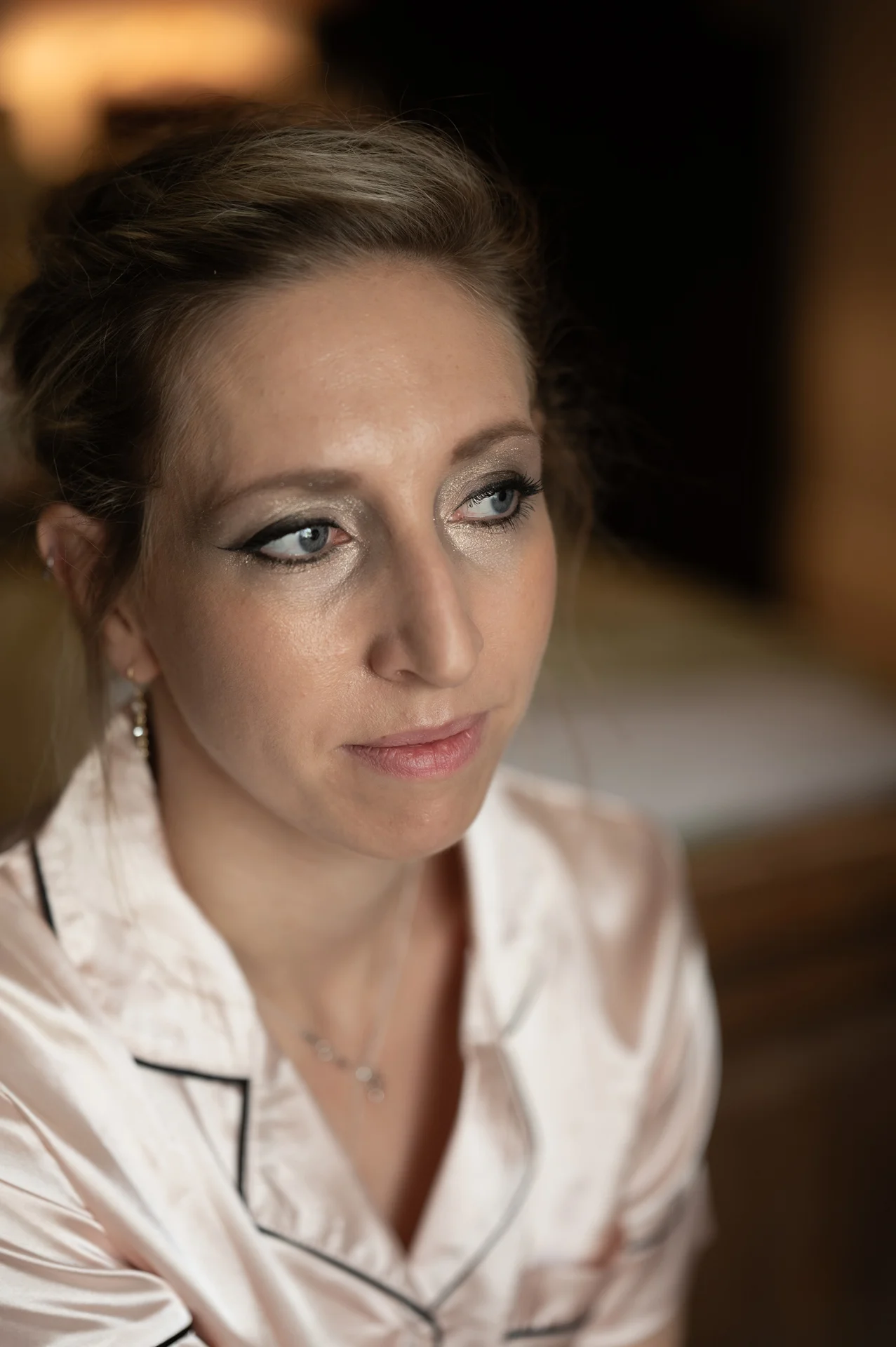 Close-up portrait of a bride looking thoughtfully away during bridal preparations while wearing a silk pyjama top and elegant makeup.