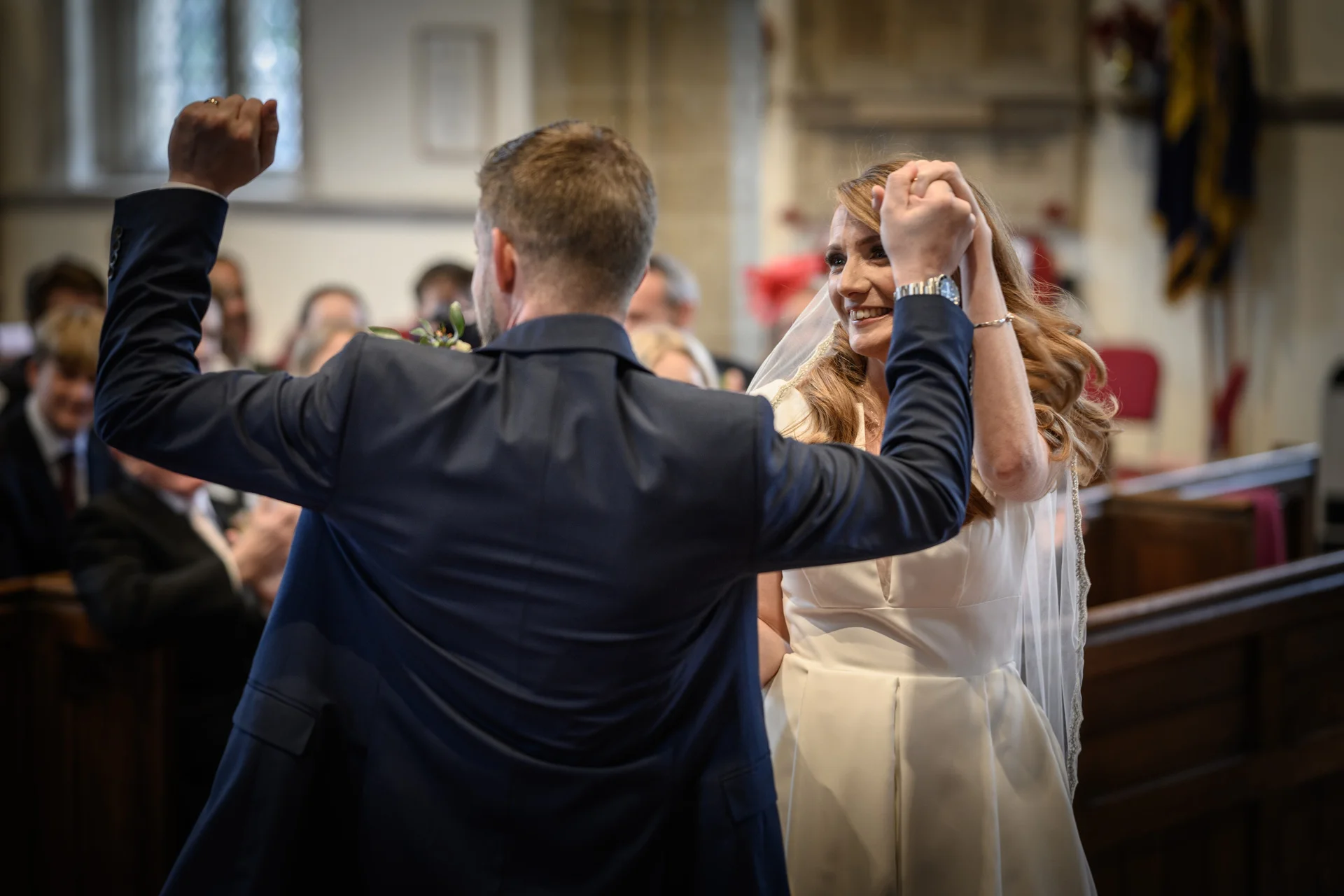 A newly married couple raise their hands in celebration as they walk down the aisle together inside a traditional church.