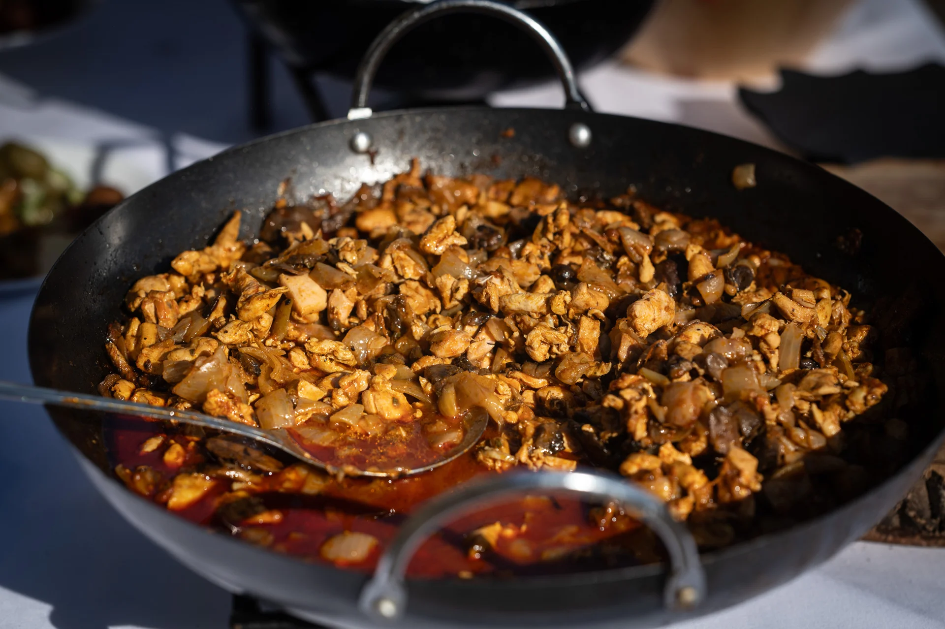 A large black pan filled with cooked chicken and vegetables sits ready for guests during a wedding catering service.