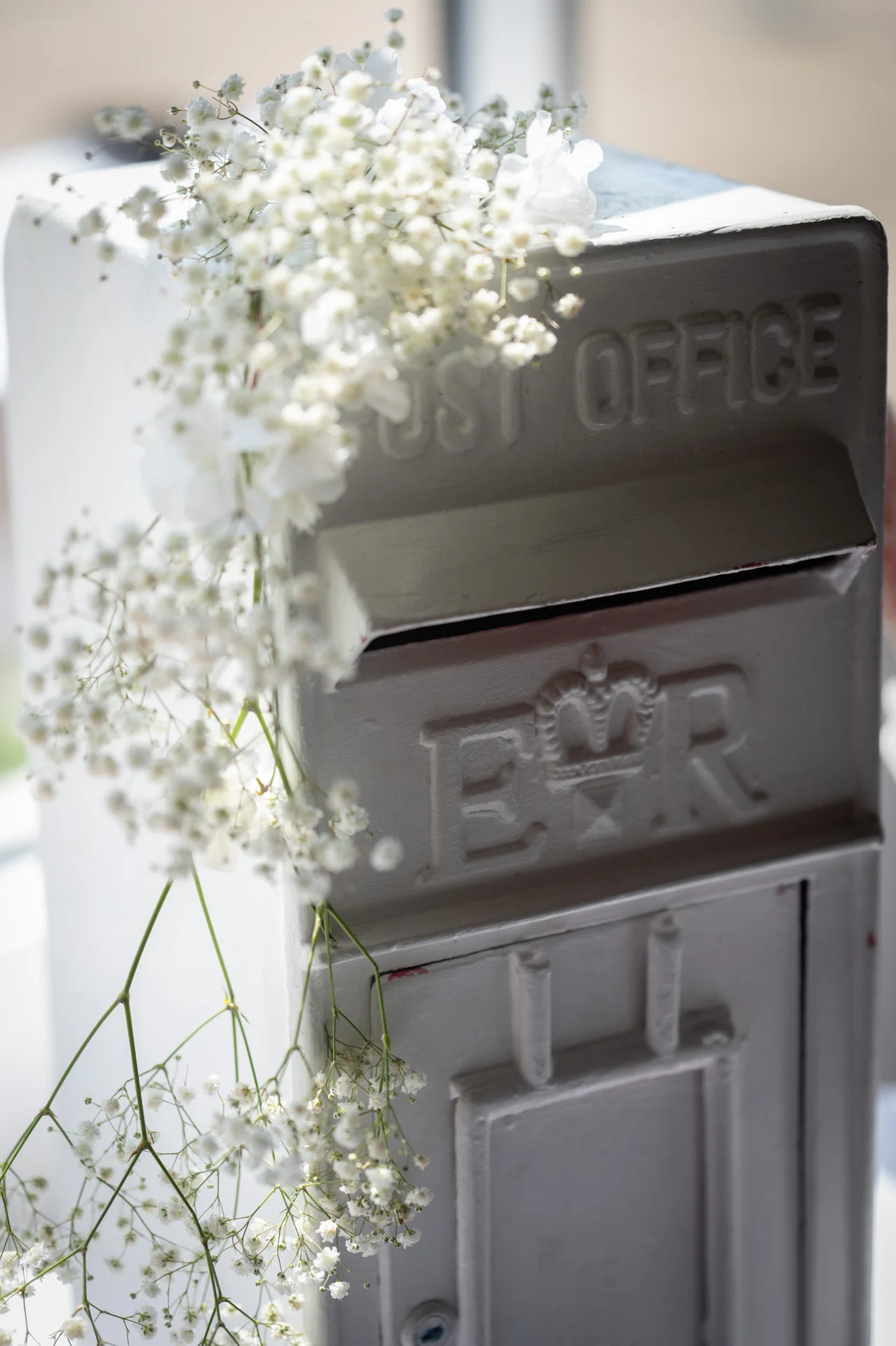 A vintage white post box decorated with delicate white baby's breath flowers sits indoors in soft natural light.
