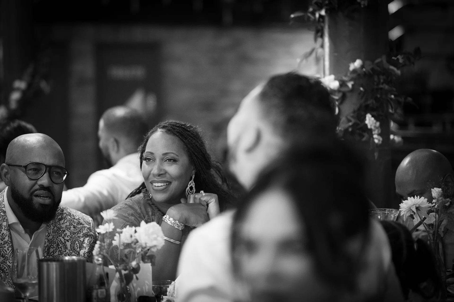 A joyful wedding guest with braided hair and statement earrings smiles while mingling with family and friends during the evening reception.