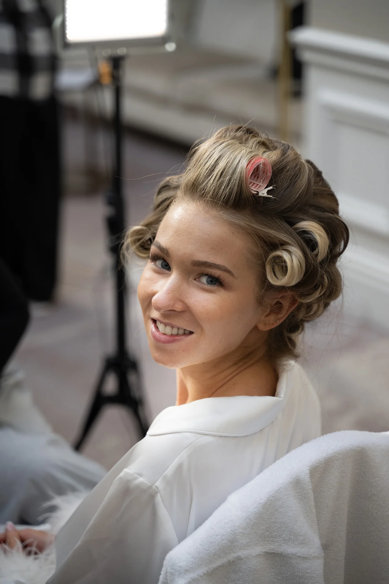 A smiling bride looks back over her shoulder while having her hair set in rollers during morning bridal preparations.