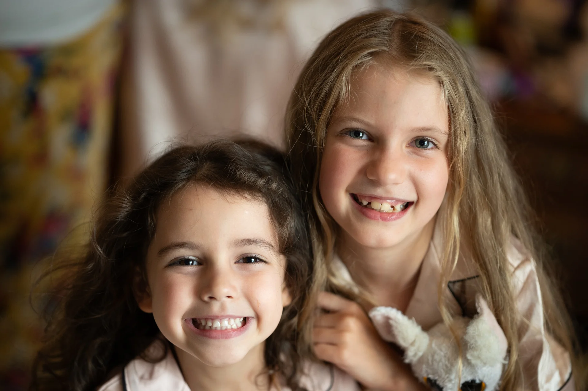 Two smiling young girls with long hair wearing matching pyjamas share a joyful moment together during wedding preparations.