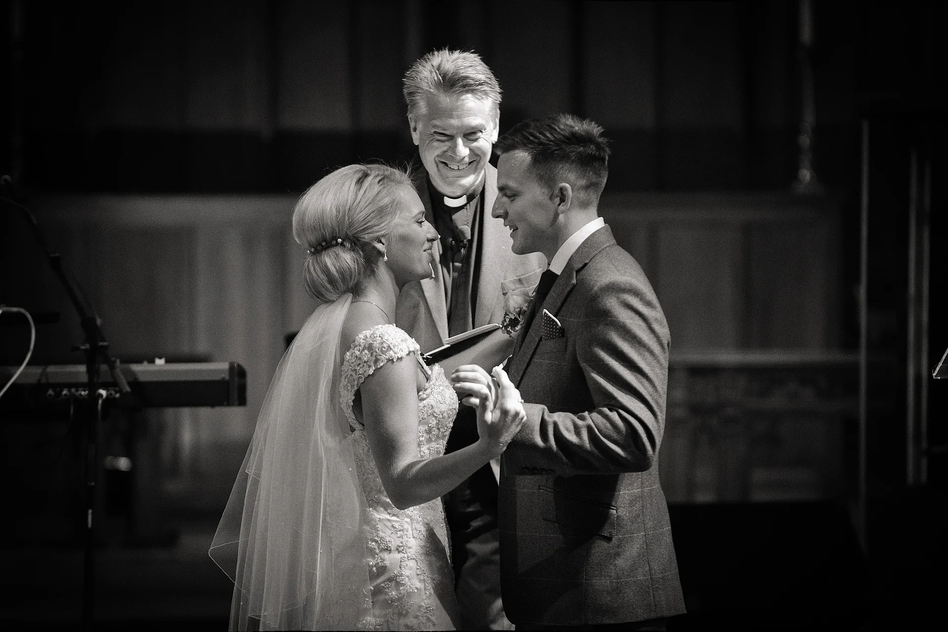 A joyous bride and groom share a tender moment during their church wedding ceremony, accompanied by a smiling clergyman standing between them.